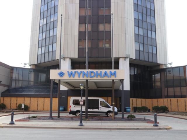 Front entrance of a multi-story Wyndham hotel with a white van parked under the porte-cochère and a blue Wyndham sign above the doorway