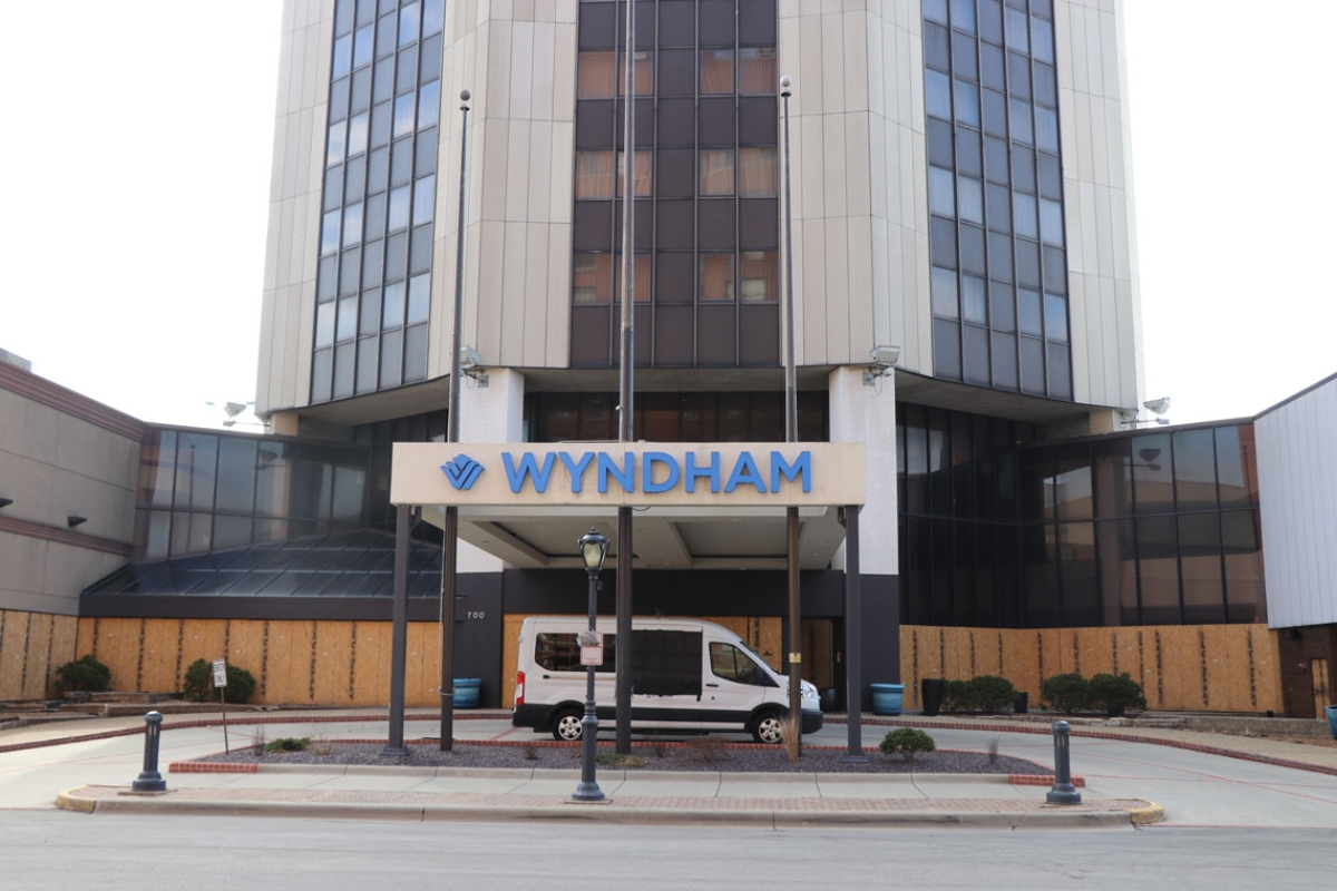 Front entrance of a multi-story Wyndham hotel with a white van parked under the porte-cochère and a blue Wyndham sign above the doorway