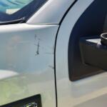 White pickup truck door with several scratches and a small dent near the front edge; '1500' badge visible.