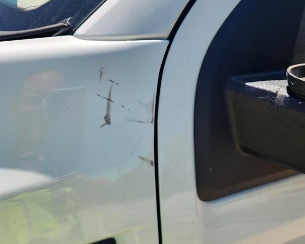 White pickup truck door with several scratches and a small dent near the front edge; '1500' badge visible.