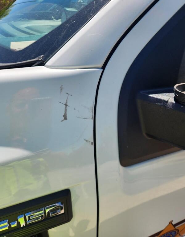 White pickup truck door with several scratches and a small dent near the front edge; '1500' badge visible.