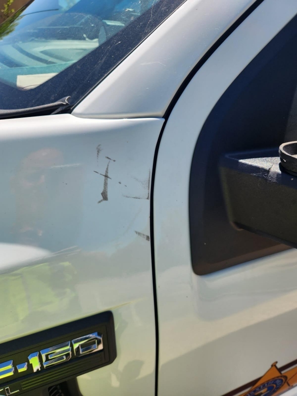 White pickup truck door with several scratches and a small dent near the front edge; '1500' badge visible.