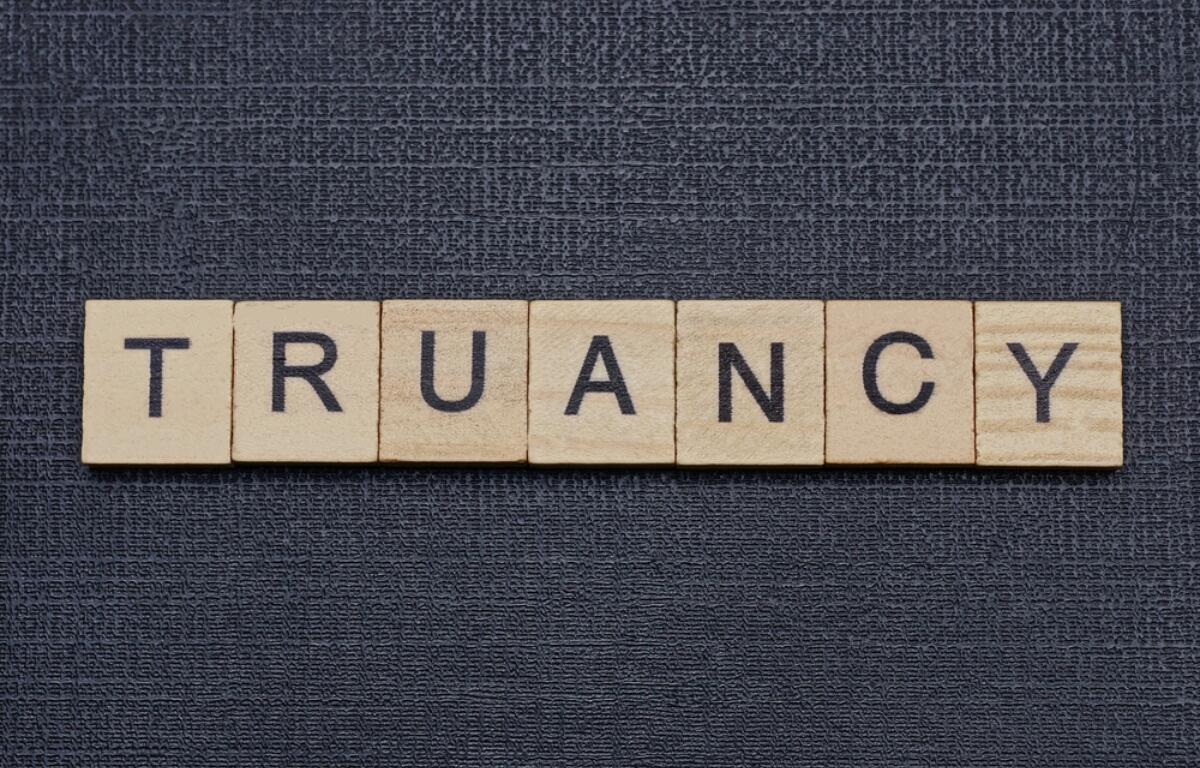 Wooden letter tiles spell the word 'TRUANCY' on a dark textured background.