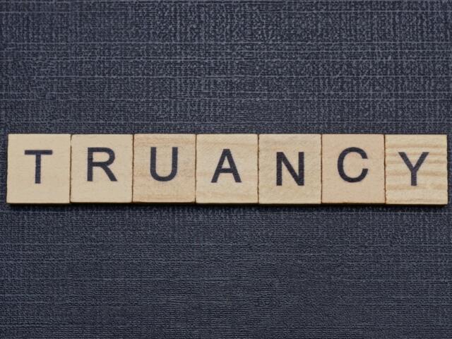 Wooden letter tiles spell the word 'TRUANCY' on a dark textured background.