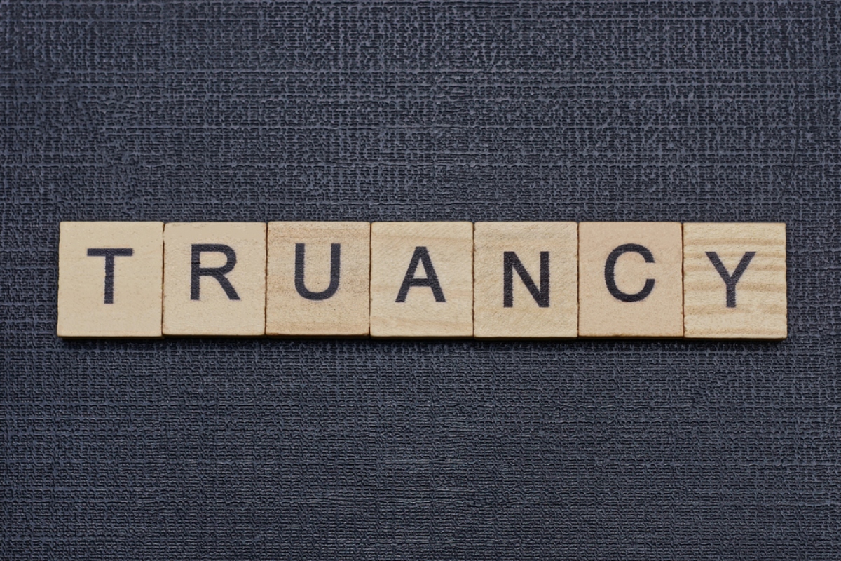 Wooden letter tiles spell the word 'TRUANCY' on a dark textured background.
