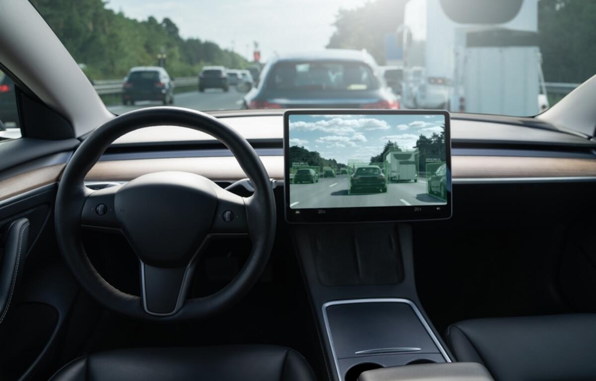 Interior of a modern car showing a steering wheel and a large central touchscreen displaying a highway with other vehicles ahead.