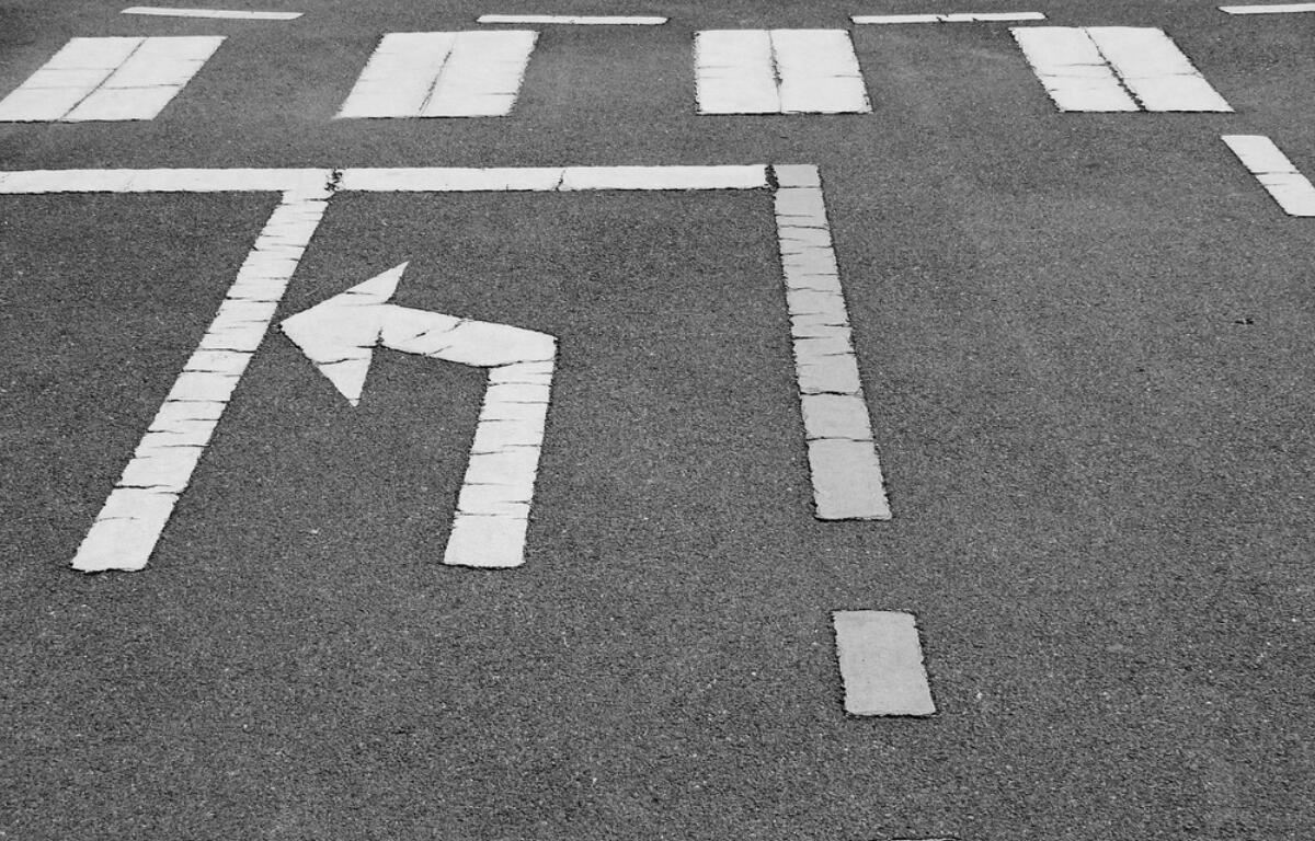 Left-turn arrow painted on dark asphalt with surrounding lane markings in the background