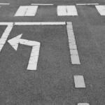 Left-turn arrow painted on dark asphalt with surrounding lane markings in the background