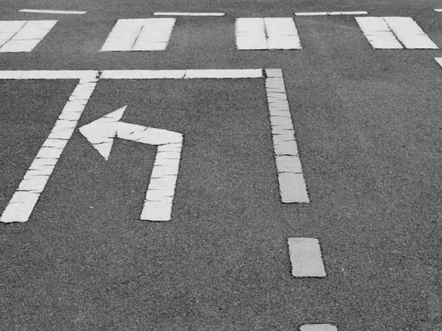 Left-turn arrow painted on dark asphalt with surrounding lane markings in the background