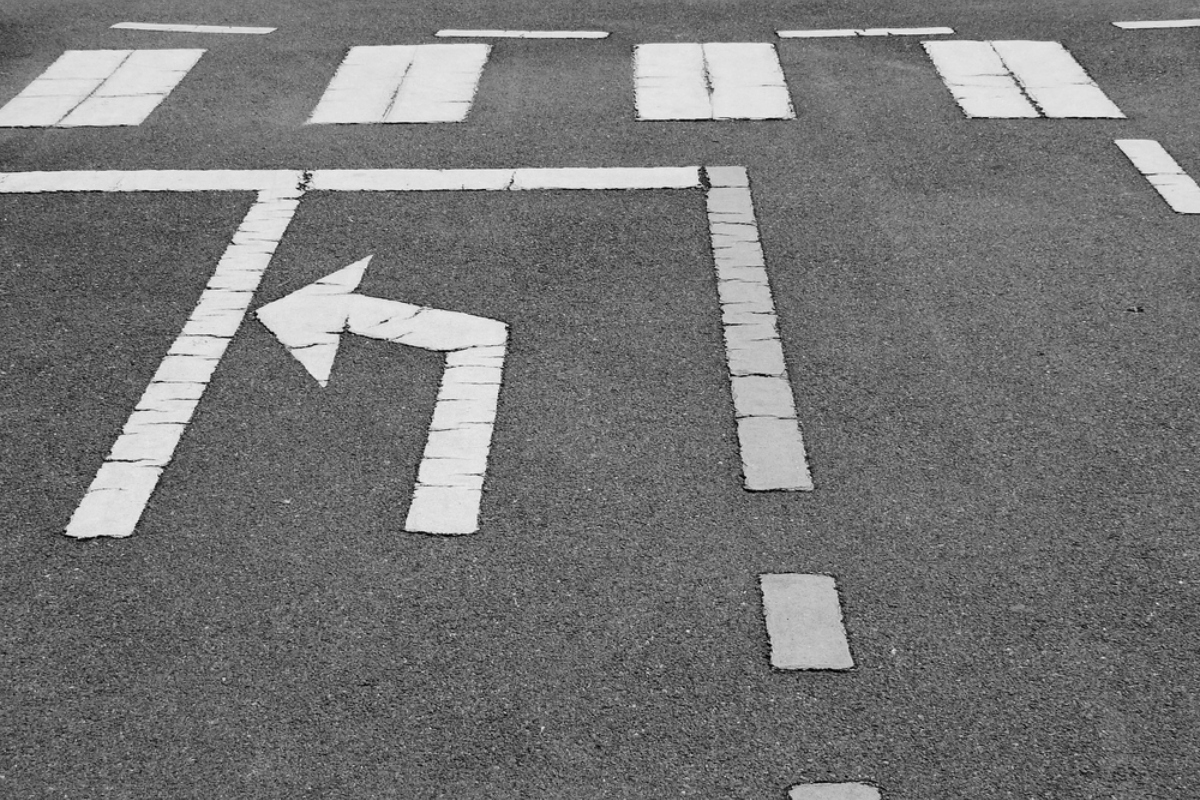 Left-turn arrow painted on dark asphalt with surrounding lane markings in the background