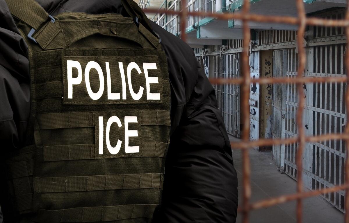 An Immigration and Customs Enforcement (ICE) officer stands in front of a dilapidated detention facility gate.