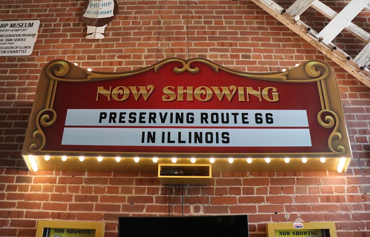 A marquee-style sign inside the brick-walled museum read “Now Showing: Preserving Route 66 in Illinois,” lit with bulbs. (Medill Illinois News Bureau photo by Chloe Park)