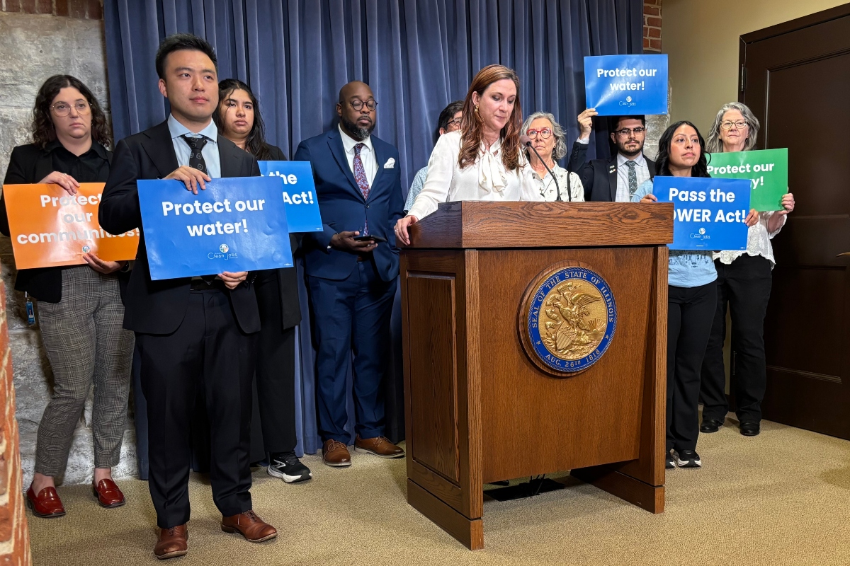 Diverse group at a press conference behind a podium, holding signs that urge Protect our water and Pass the POWER Act.