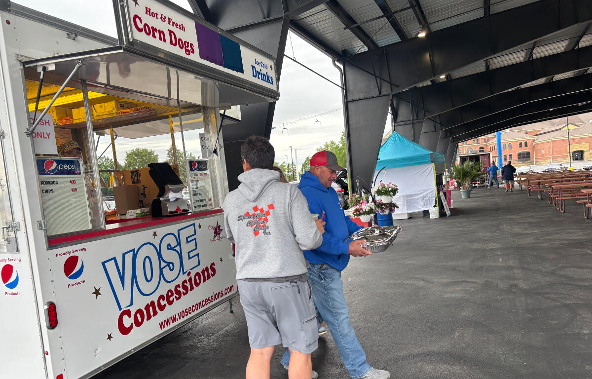 Concession trailer labeled 'Vose Concessions' at an outdoor event with two men near the window, one in a gray hoodie and the other in a blue jacket holding a foil tray.