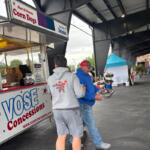 Concession trailer labeled 'Vose Concessions' at an outdoor event with two men near the window, one in a gray hoodie and the other in a blue jacket holding a foil tray.