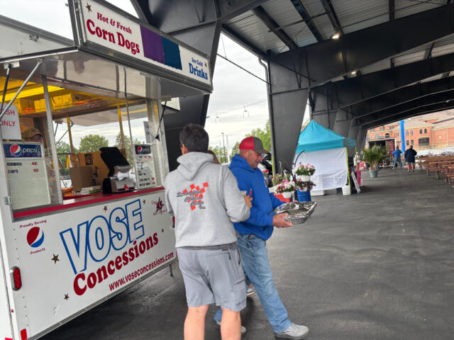 Concession trailer labeled 'Vose Concessions' at an outdoor event with two men near the window, one in a gray hoodie and the other in a blue jacket holding a foil tray.