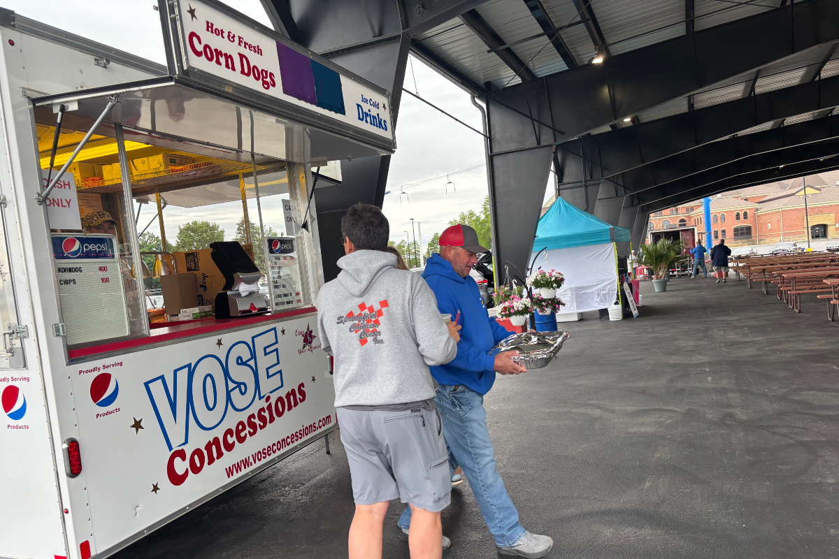 Concession trailer labeled 'Vose Concessions' at an outdoor event with two men near the window, one in a gray hoodie and the other in a blue jacket holding a foil tray.