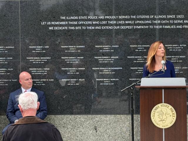 Michelle Hanneken, right, speaks at a memorial service held at the Illinois State Police Memorial Wall Wednesday, May 6, while Illinois State Police Heritage Foundation Executive Director Jarod Ingebrigtsen listens.