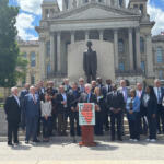 Group of officials and supporters on the steps in front of a statue at a government building, giving a press conference for Restore LGDF.