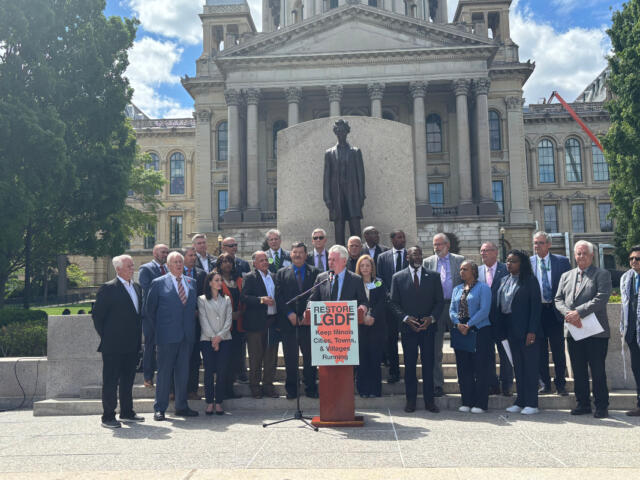 Group of officials and supporters on the steps in front of a statue at a government building, giving a press conference for Restore LGDF.