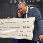 Two people in formal attire hold a large ceremonial check from the Central Illinois Building & Construction Trades Council, dated May 8, 2026, for $150,000 to 'Friends of Misty Busher' with signatures visible, as another man applauds in the background.