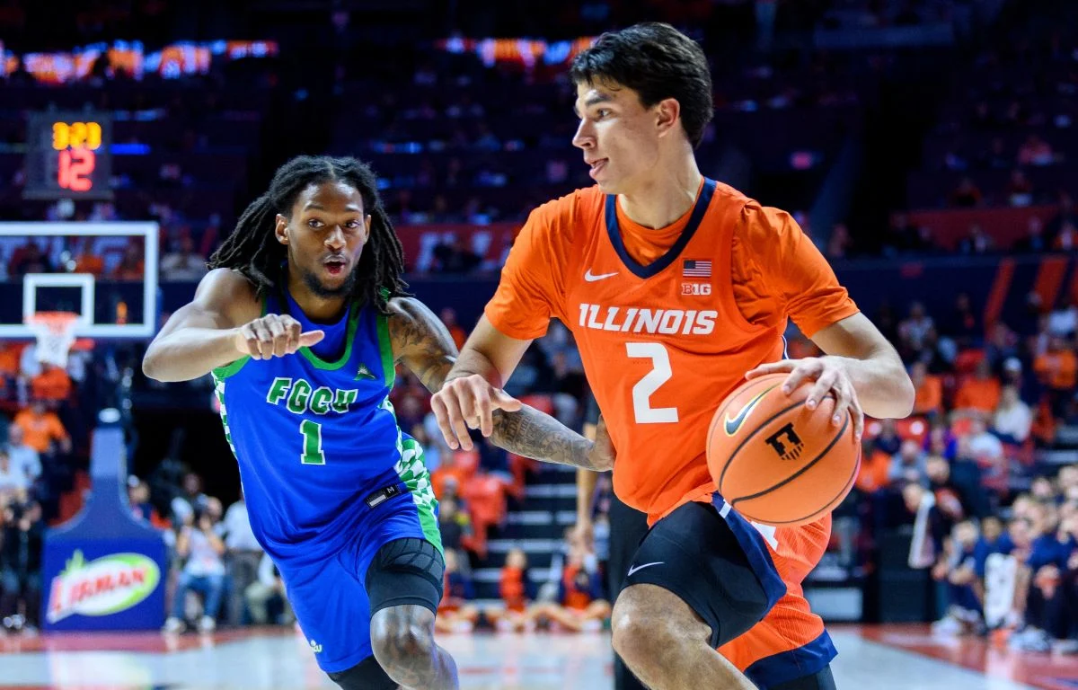 Two college basketball players sprint toward the hoop during a fast break; Illinois in orange and FGCU in blue facing off on a crowded court.