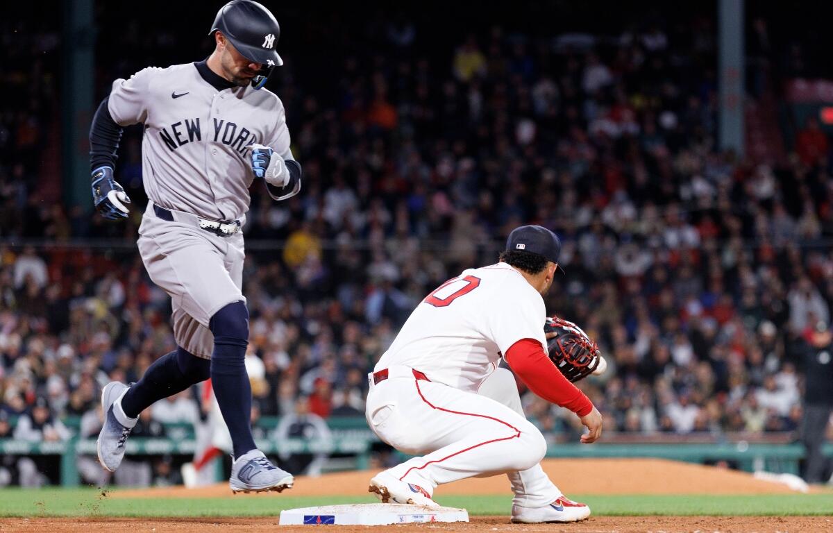 Yankees baserunner in gray uniform races toward second base as a Red Sox fielder guards the bag; crowded ballpark in background.