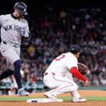 Yankees baserunner in gray uniform races toward second base as a Red Sox fielder guards the bag; crowded ballpark in background.