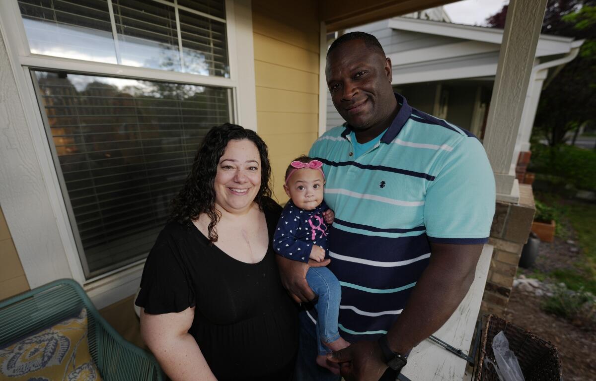 Farra White poses with her 1-year-old daughter, Olivia, and husband Marlon White outside their residence Thursday, May 7, 2026, in Fort Collins, Colo. (AP Photo/David Zalubowski)
