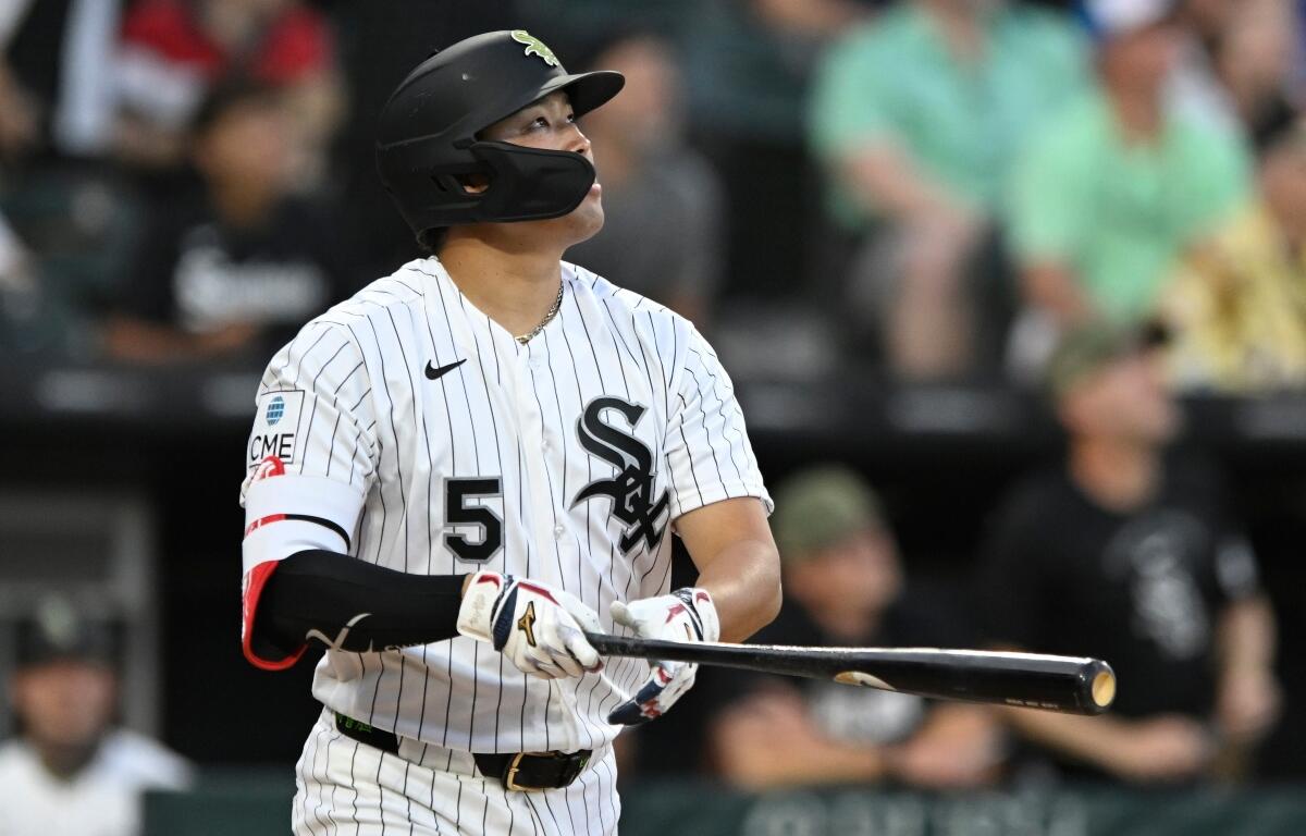 Baseball player in White Sox pinstripe uniform swings a bat during a game, wearing a protective face mask and helmet with number 5 visible.