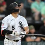 Baseball player in White Sox pinstripe uniform swings a bat during a game, wearing a protective face mask and helmet with number 5 visible.