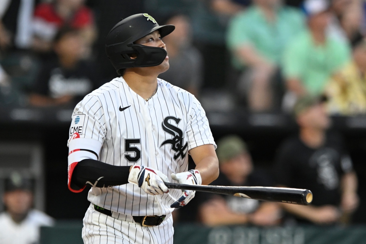 Baseball player in White Sox pinstripe uniform swings a bat during a game, wearing a protective face mask and helmet with number 5 visible.