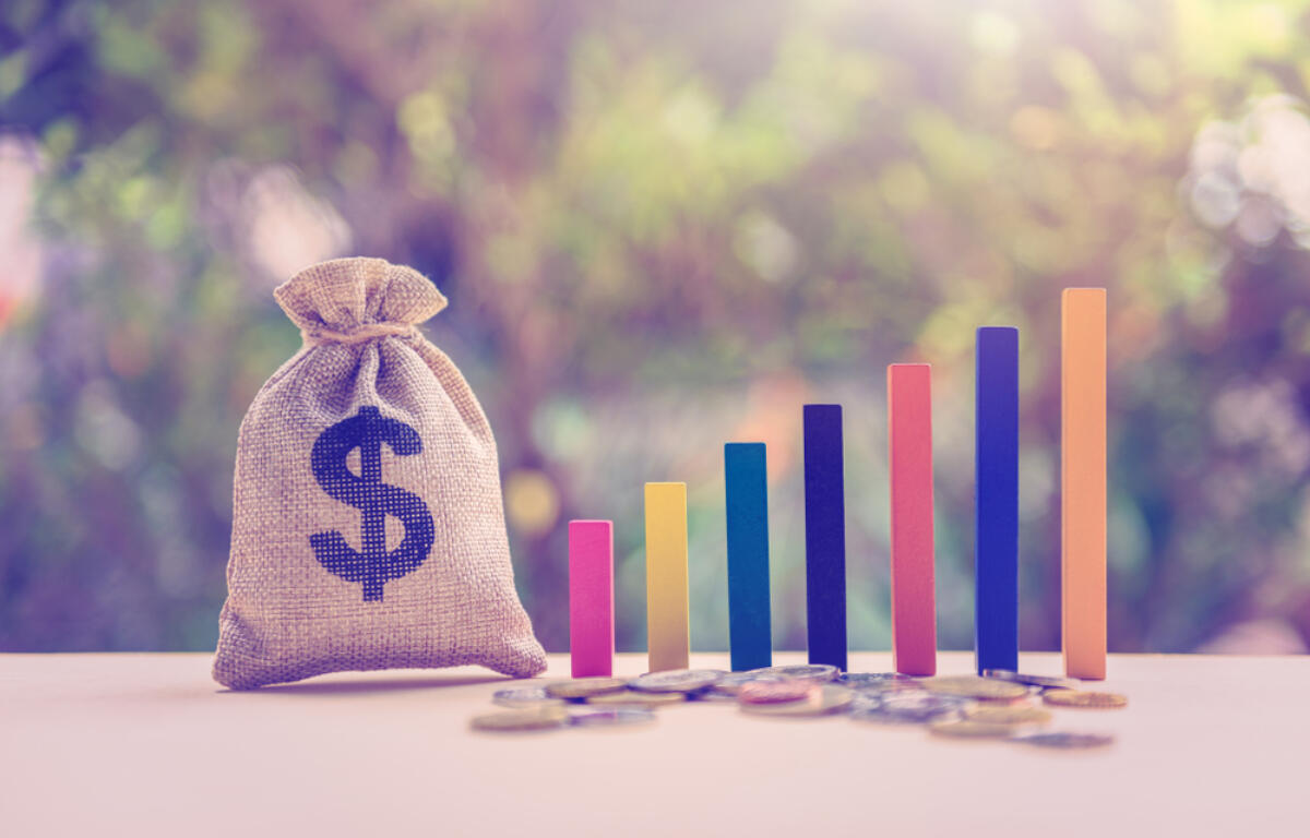 Money bag with a dollar sign beside a rising multicolored bar chart and coins, symbolizing financial growth and savings growth.