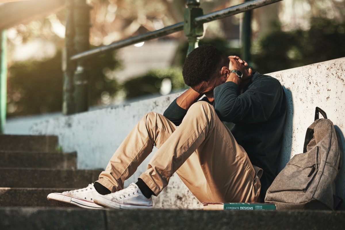Student, mental health and depression with anxiety, burnout and sad for exam results, fail or mistake while sitting outdoor. Young man, stress and tired and depressed on university or college campus