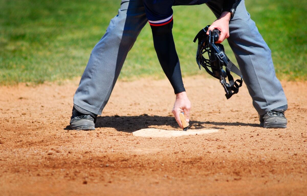 View of Baseball Umpire Brushing Off and Cleaning Home Plate with Hand Brush for Ball Game