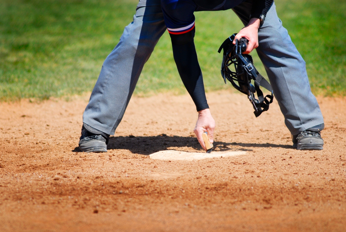 View of Baseball Umpire Brushing Off and Cleaning Home Plate with Hand Brush for Ball Game