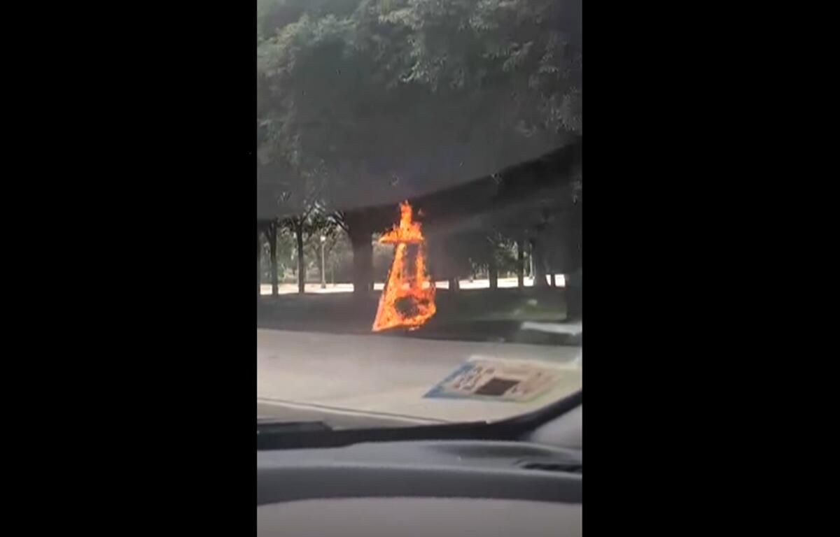 This grab from a video taken by motorist Keinika Carlton shows a wooden cross engulfed in bright orange flames as it leans against a tree in Grant Park, Chicago, Illinois, on Tuesday, July 9, 2026.(Keinika Carlton via AP)