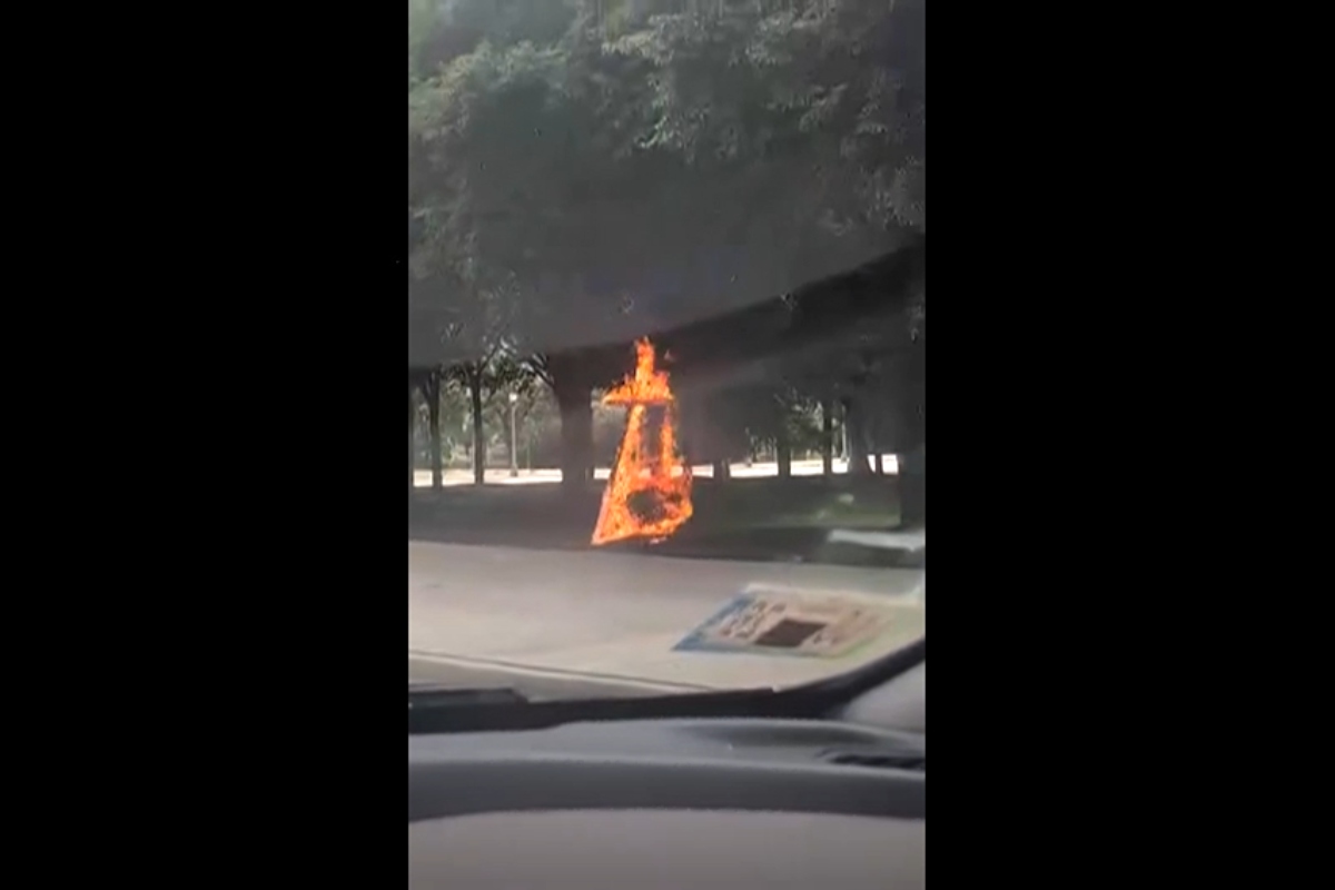 This grab from a video taken by motorist Keinika Carlton shows a wooden cross engulfed in bright orange flames as it leans against a tree in Grant Park, Chicago, Illinois, on Tuesday, July 9, 2026.(Keinika Carlton via AP)