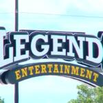 Legends Entertainment sign with large white letters and a curved yellow 'ENTERTAINMENT' banner beneath it against a blue sky.