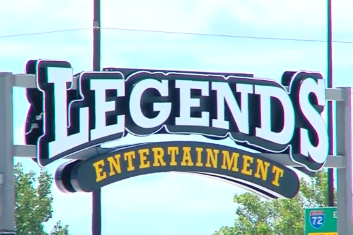 Legends Entertainment sign with large white letters and a curved yellow 'ENTERTAINMENT' banner beneath it against a blue sky.