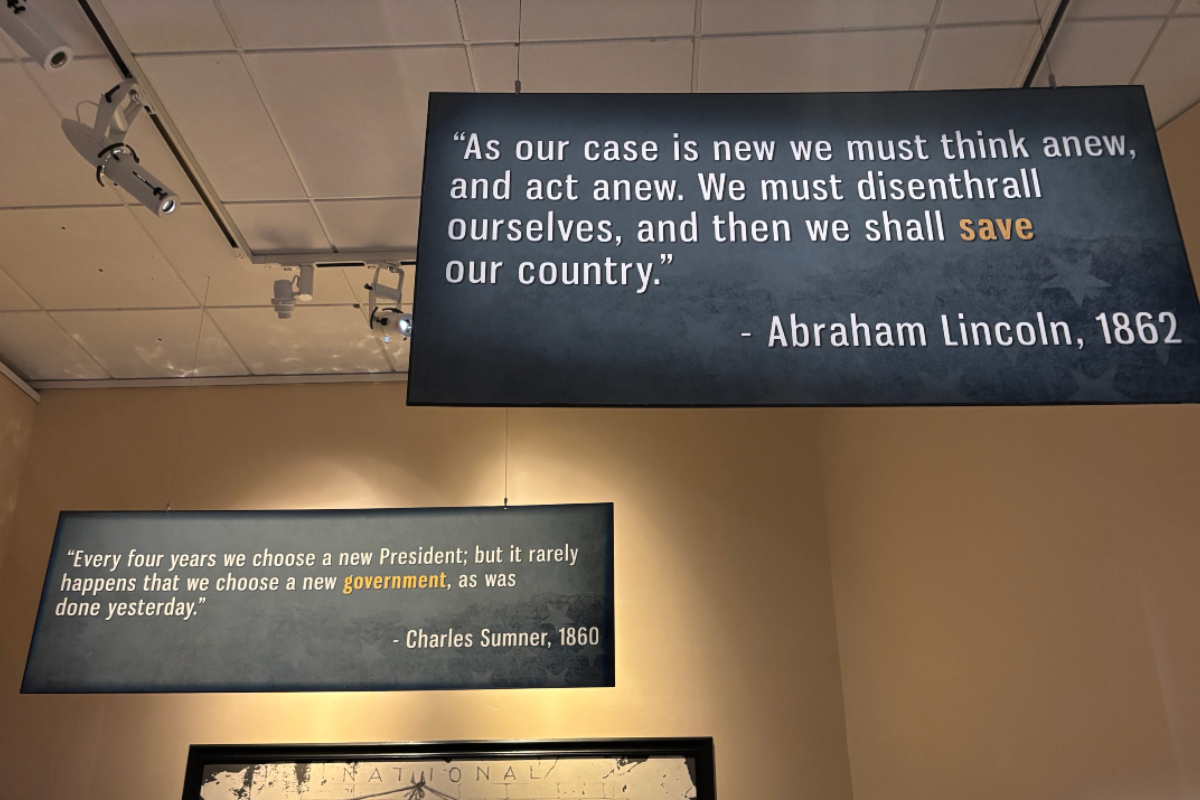 Two hanging blue quote boards on a museum wall; Lincoln (1862) quote about thinking anew and saving the country, and Sumner (1860) quote about government.