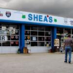 Front of Shea's shop along Route 66, blue trim, large windows with decals; two men approach the entrance.