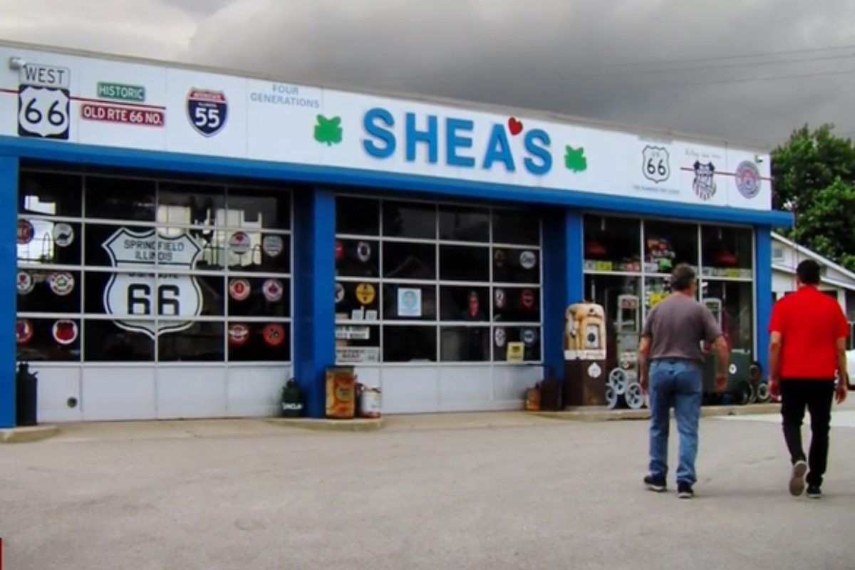 Front of Shea's shop along Route 66, blue trim, large windows with decals; two men approach the entrance.