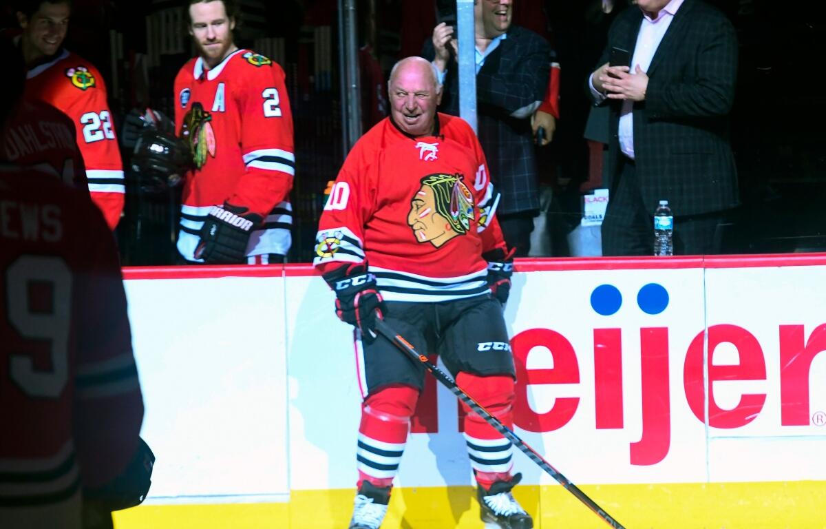 Center ice hockey player in a red Chicago Blackhawks jersey (number 10) smiles while holding a stick near the boards.