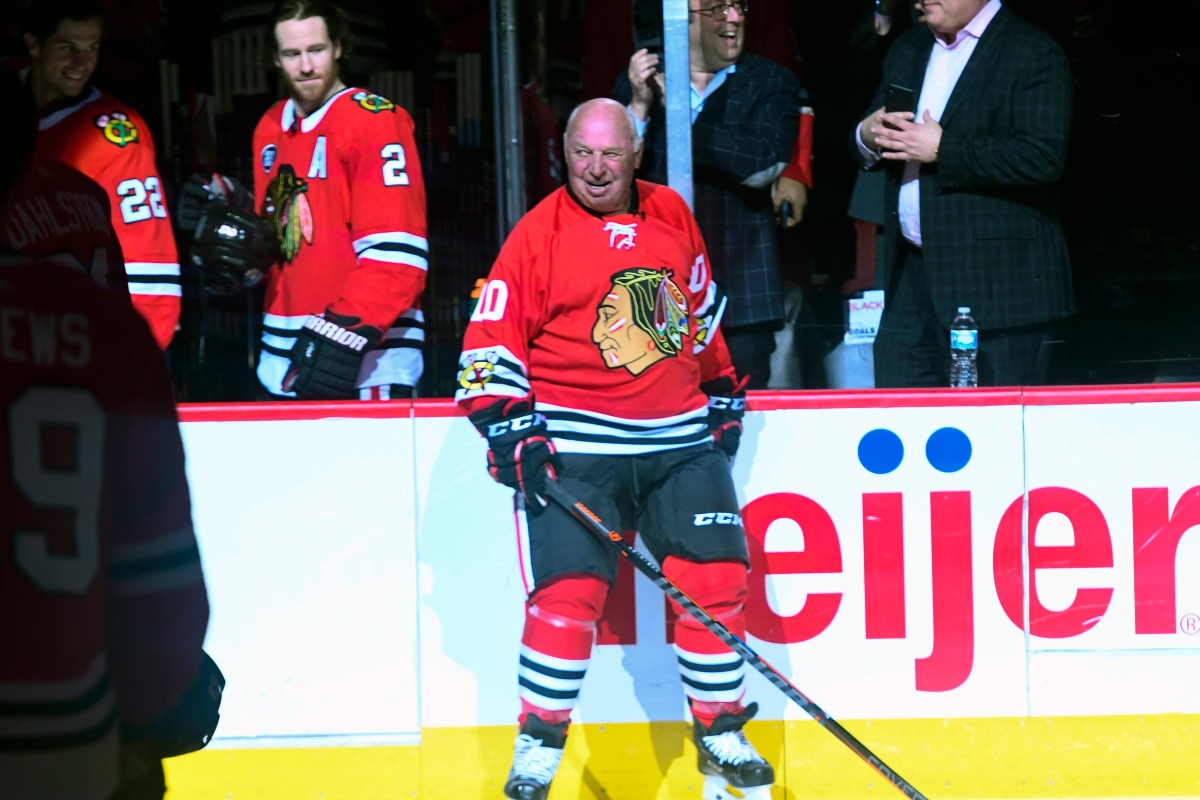 Center ice hockey player in a red Chicago Blackhawks jersey (number 10) smiles while holding a stick near the boards.