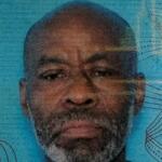 Close-up portrait of a middle-aged man with a gray beard, looking straight ahead, against a blue textured background.