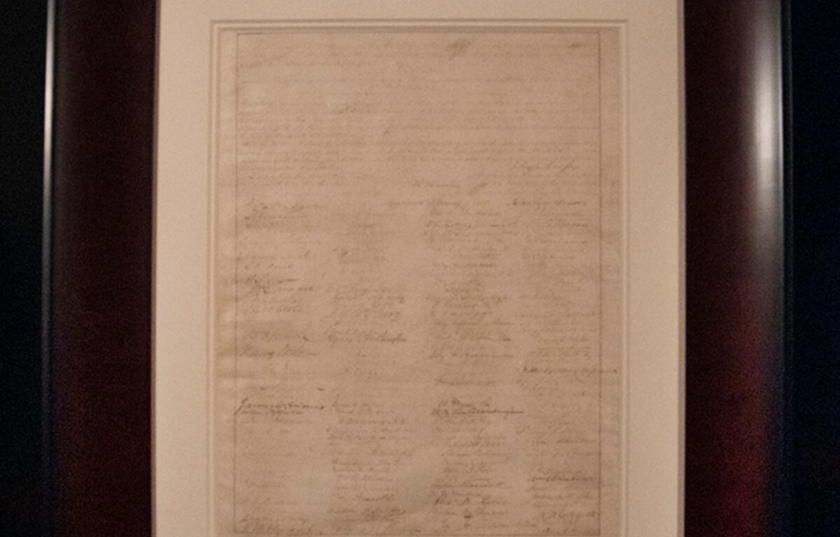 Framed parchment with dense handwritten text displayed on a wall/gallery setting.