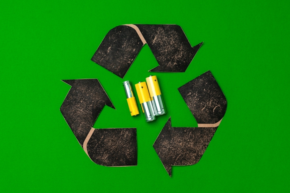 Recycling symbol formed by four black arrow shapes on a bright green background, with three batteries in the center.