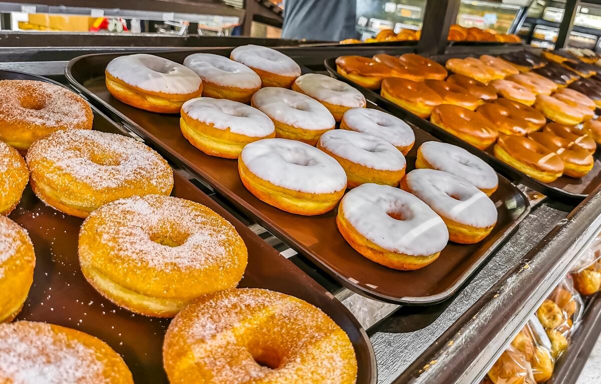 Assorted donuts on display trays in a bakery, including sugar-dusted ring donuts and white-glazed donuts.