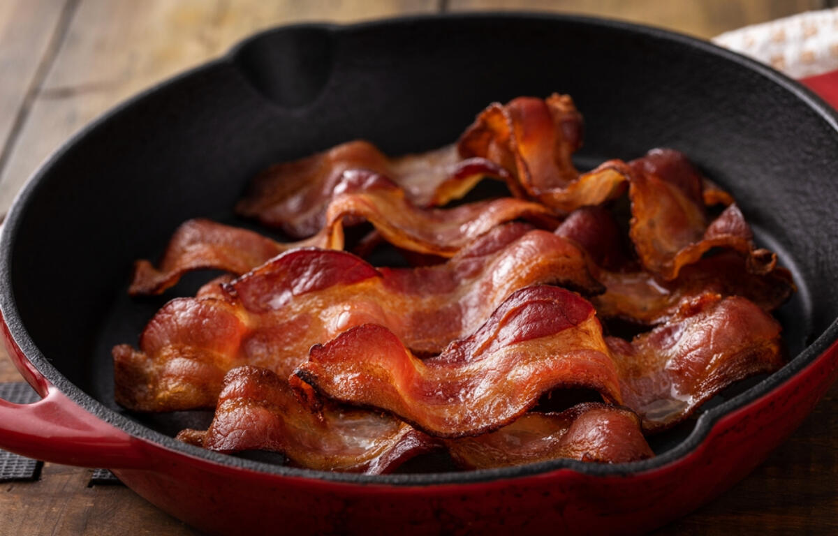 Crispy bacon slices arranged in a red cast-iron skillet on a wooden table.